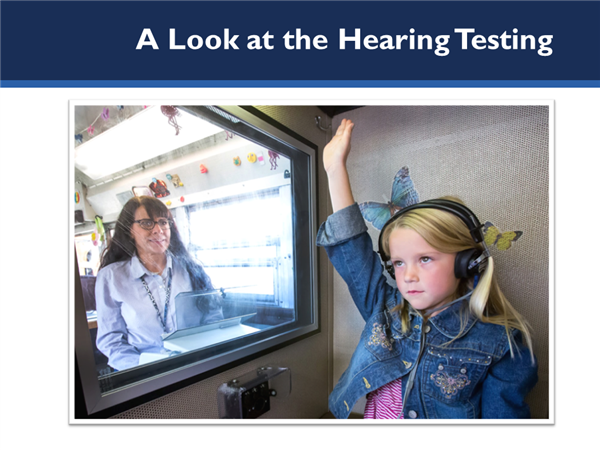 Picture of girl in testing booth with audiologist looking on